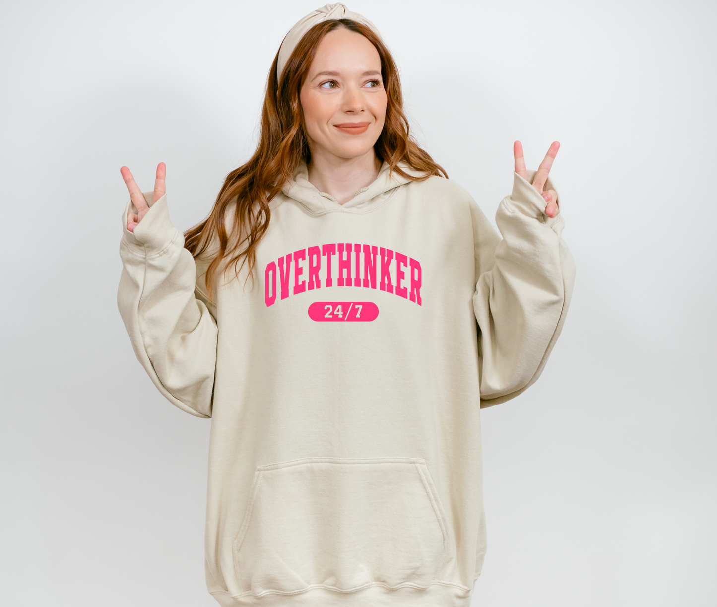 Person wearing a beige hoodie with 'OVERTHINKER 24/7' text on a white background