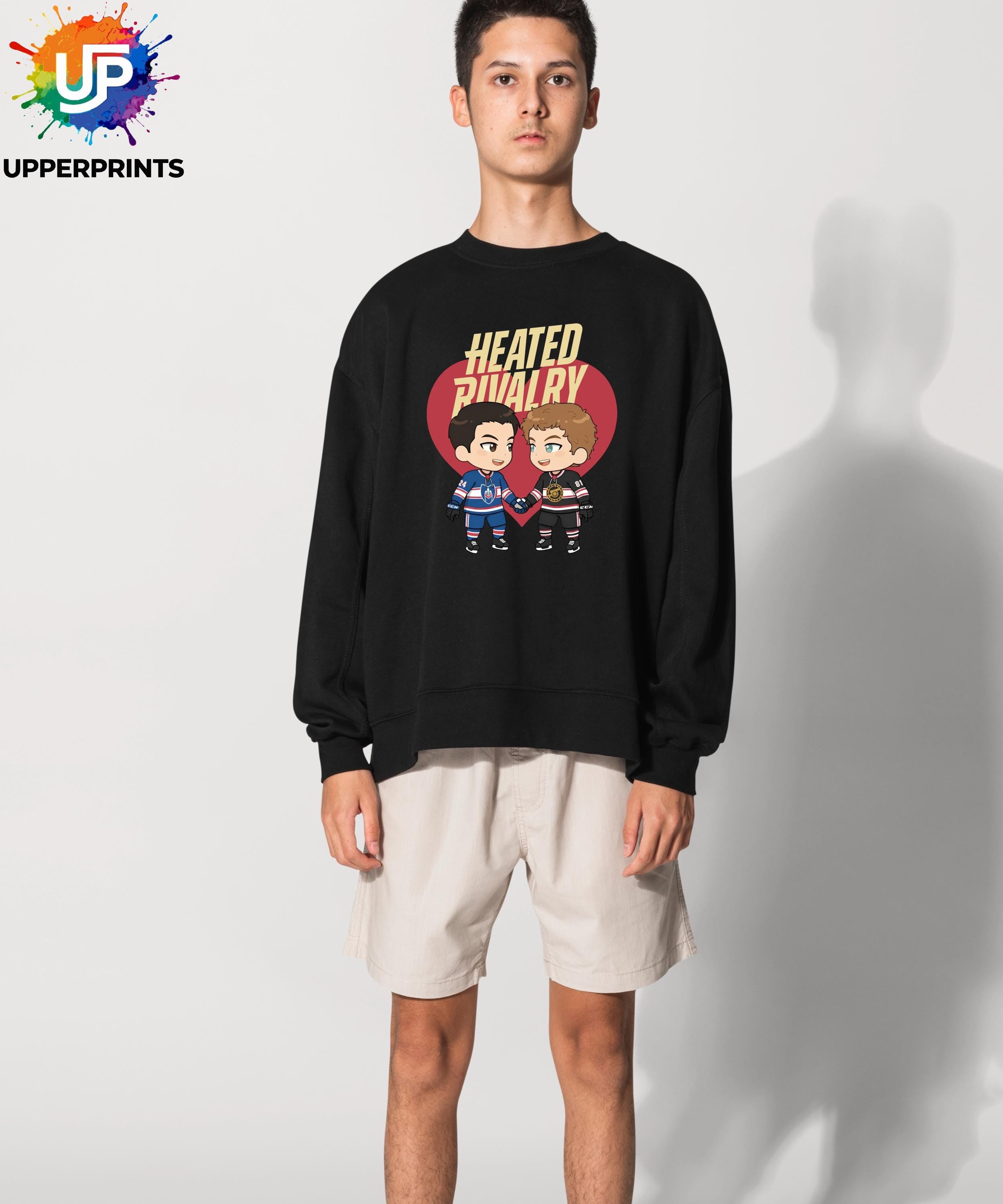 May include: Black sweatshirt featuring the text "HEATED RIVALRY" above a cartoon image of two hockey players holding hands inside a red heart. The sweatshirt is worn by a person wearing beige shorts.